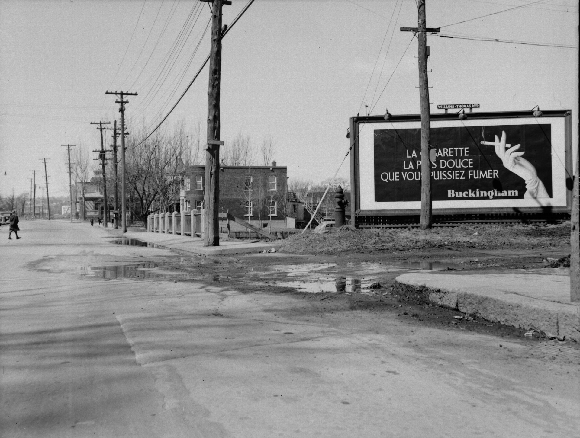 Il s'agit d'un négatif représentant une rue avec, à côté une affiche publicitaire de la cigarette Buckingham. On peut y lire, sur l'affiche : " La cigarette la plus douce que vous puissiez fumer. Buckingham ".
