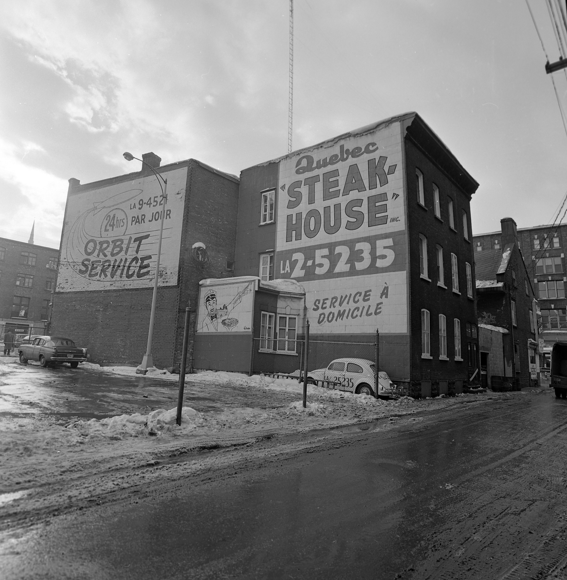 Il s'agit d'un négatif représentant des enseignes commerciales de Orbit Service et de Quebec SteakHouse sur la rue Fleurie dans le quartier St-Roch.