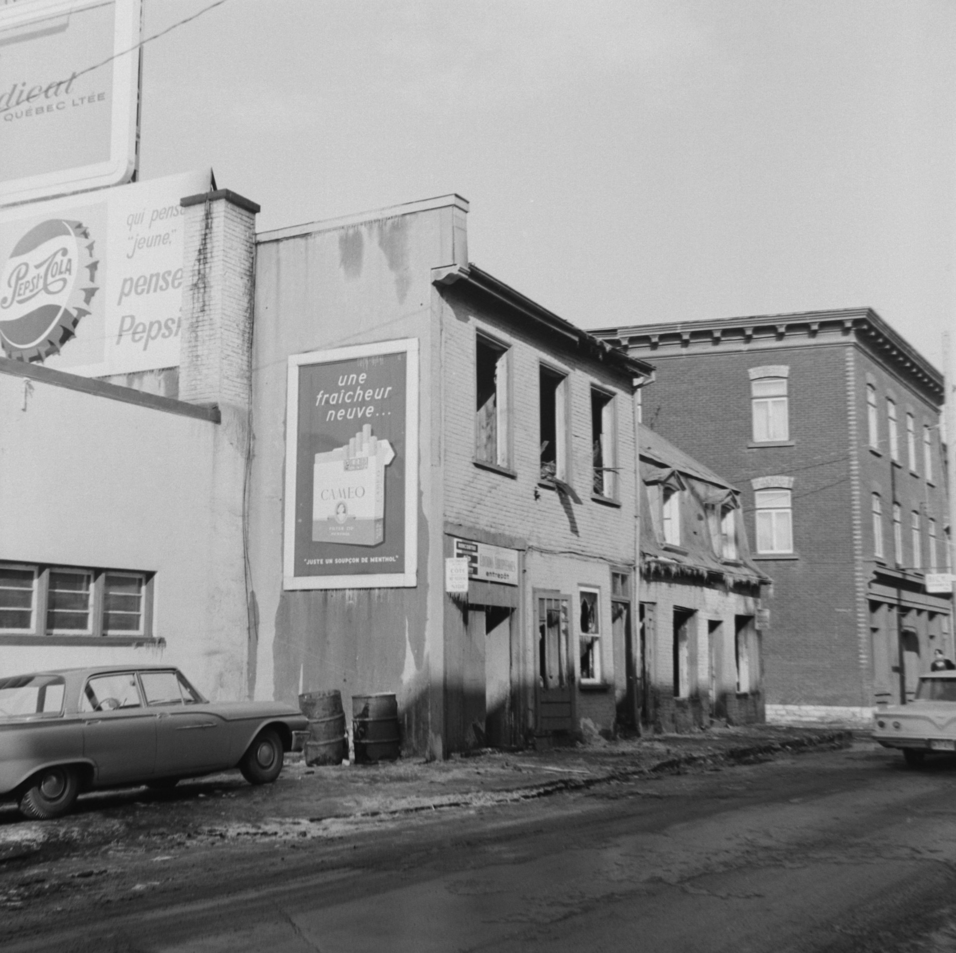 Il s'agit d'un négatif représentant des affiches publicitaires de Pepsi Cola et des Cigarettes Cameo, qui se trouvent sur un édifice incendié à l'intersection du boulevard Charest et de la rue St-Vallier dans le quartier St-Sauveur.